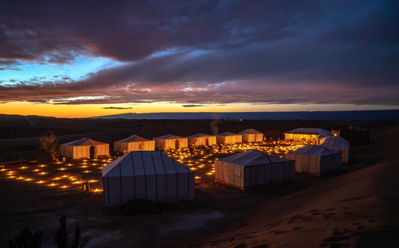 Luxury desert glamping tents illuminated by warm candlelight under a starry night sky.