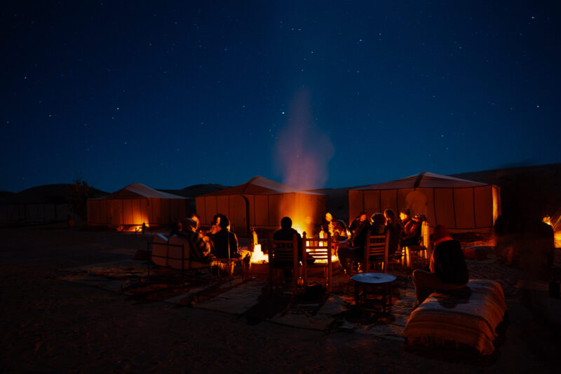 Campfire smoke rising above the stunning desert camp as stars twinkle above the tents
