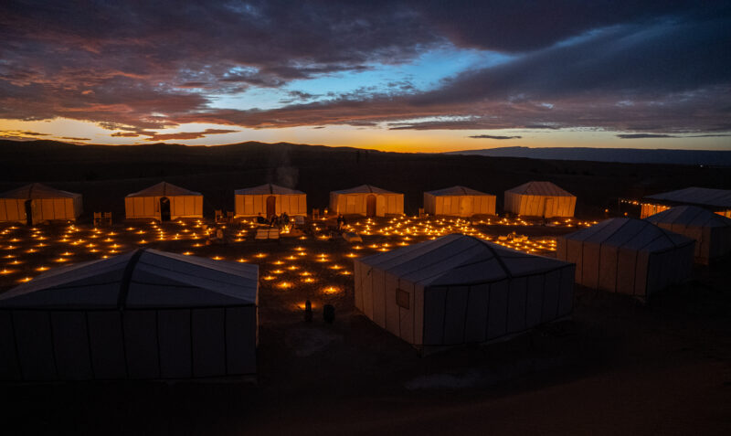 Luxury desert glamping tents illuminated by warm candlelight under a starry night sky.